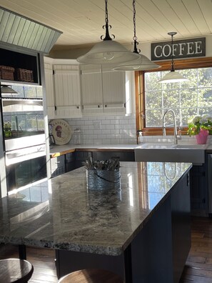 A kitchen with white cabinets, a marble countertop, a hanging light fixture, and a window with a view of trees. - Mountain View Acreage near Sylvan Lake | Huge Lit Patio, BBQ Bar & Horses! (Red Deer County)