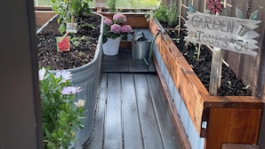 Un invernadero con bancales elevados, un letrero de madera que dice 'GARDEN TOUR' y un aviso que advierte contra alterar las malas hierbas.