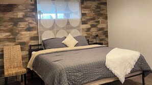 Un dormitorio con cama, una silla y una ventana con cortinas.