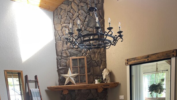 Un salón con chimenea de piedra, sofá de cuero, sillón blanco y una mesa de centro de madera.