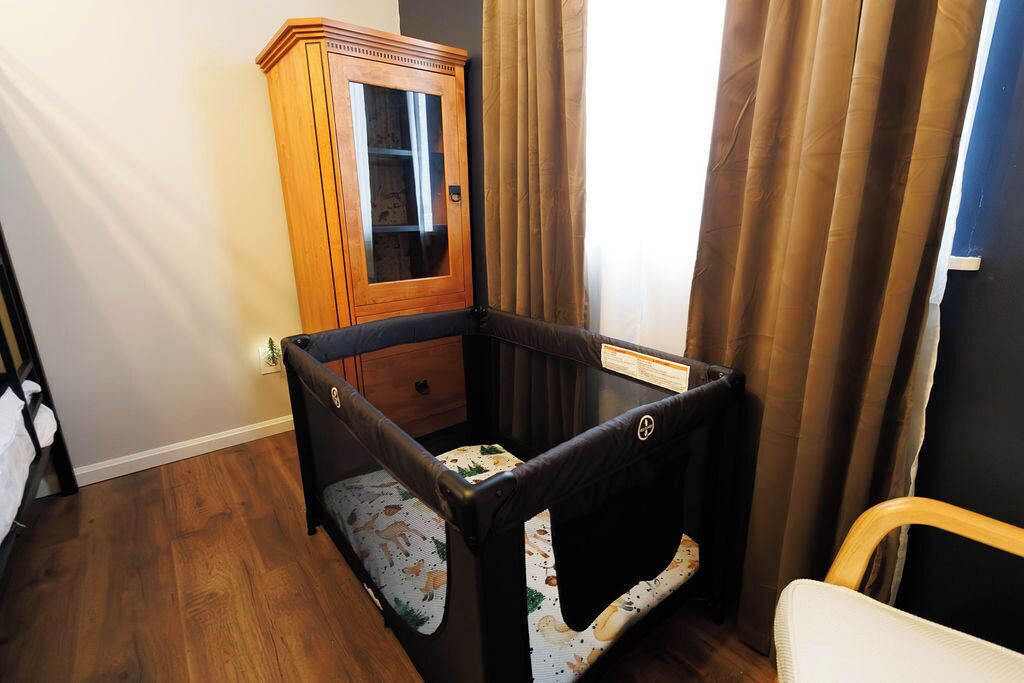 Ein Zimmer mit einem Holzkasten, einem kleinen Bett mit gemustertem Lattenrost und einem Fenster mit Vorhängen.