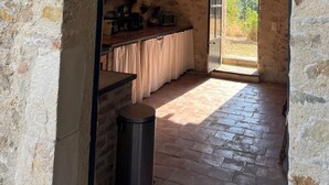 A stone-walled room with a wooden floor, a kitchen area with a counter and appliances, and a sign reading "La Cuisine". - Mas Grange Neuve (Potelières)