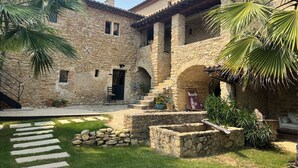 A stone building with a courtyard, featuring a stone staircase, a seating area, and palm trees. - Mas Grange Neuve (Potelières)