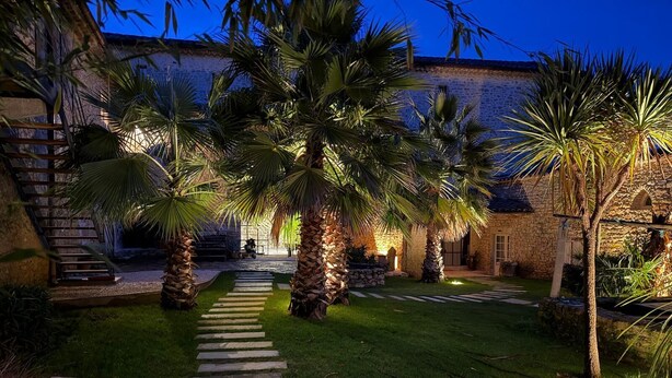 A stone building with a stone staircase leading to a door, surrounded by palm trees and a well-maintained lawn. - Mas Grange Neuve (Potelières)
