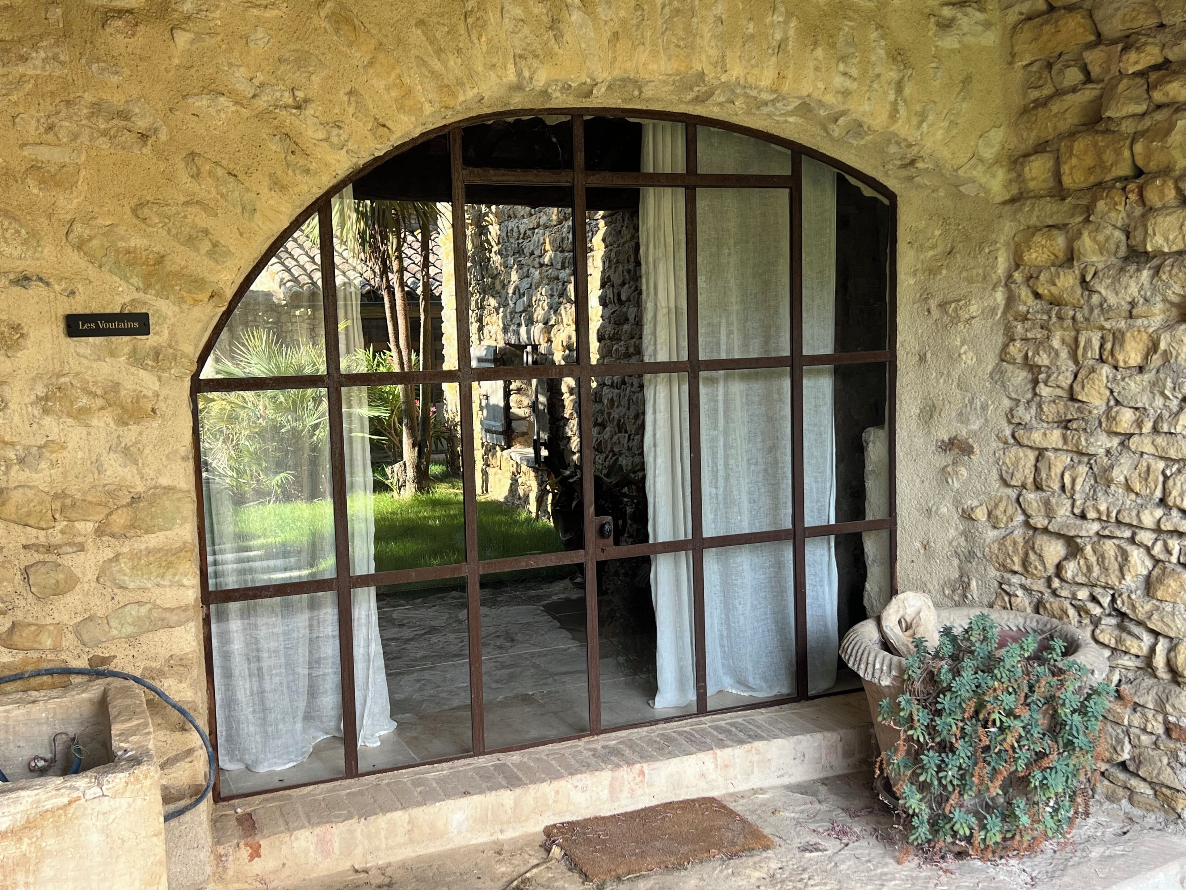 Ein Zimmer mit Steinwänden und einem großen Bogenfenster, eine kleine Stufe zum Eingang sowie ein Schild mit der Aufschrift 'Les Voutains'.