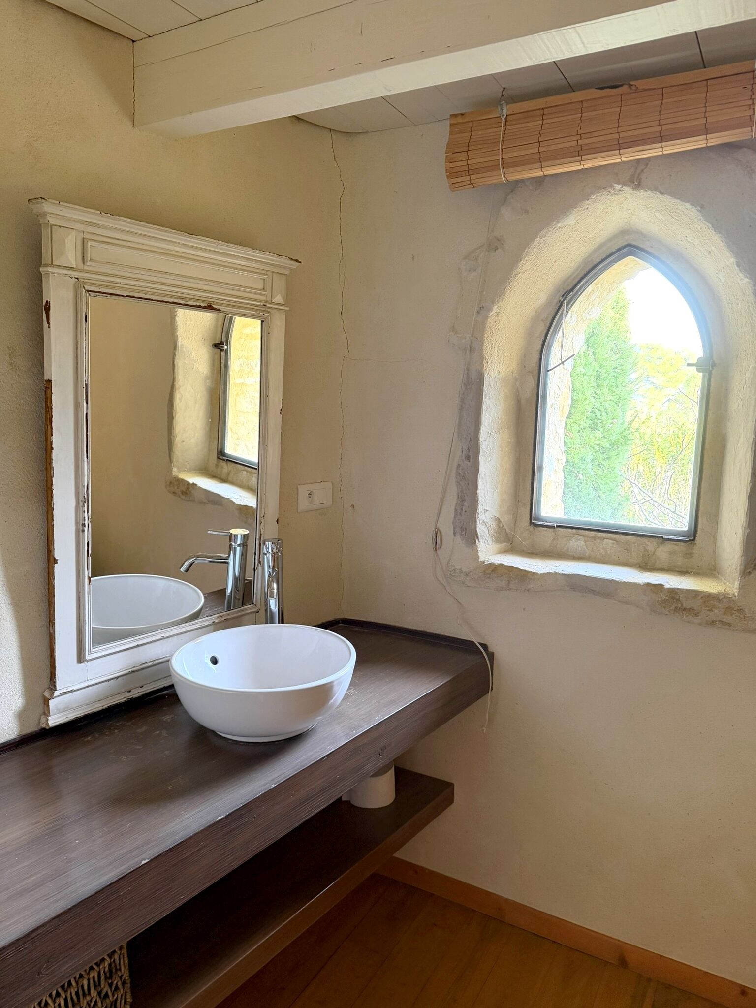 A bathroom with a white sink, a mirror, and a window with a view of greenery.