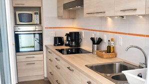 Cozinha compacta com armários de madeira clara, forno embutido, micro-ondas, cafeteira e pia.