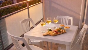 Uma mesa de varanda com cadeiras brancas, uma tábua de madeira com queijos e enchidos, e três copos de vinho branco.