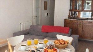 Uma área de refeições com uma mesa redonda posta para o café da manhã, incluindo croissants, frutas e bebidas.