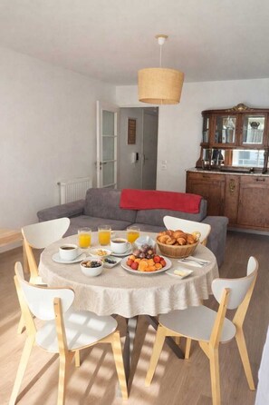 A dining area with a round table set for breakfast, including croissants, fruit, and beverages. - Bright apartment - 5-minute bike ride to the beach (Carnac)