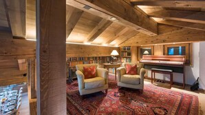 Una habitación acogedora con un piano, dos sillones, una estantería y un comedor con mesa preparada para cuatro.
