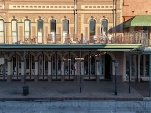 Un edificio con toldo verde, varias ventanas y un balcón con sillas y mesas.