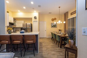 A modern kitchen with a central island, bar stools, a dining area with chairs, and a decorative plant. - TU220 - 5BR house sleeps 12 in Tuscan Hills resort (Davenport)