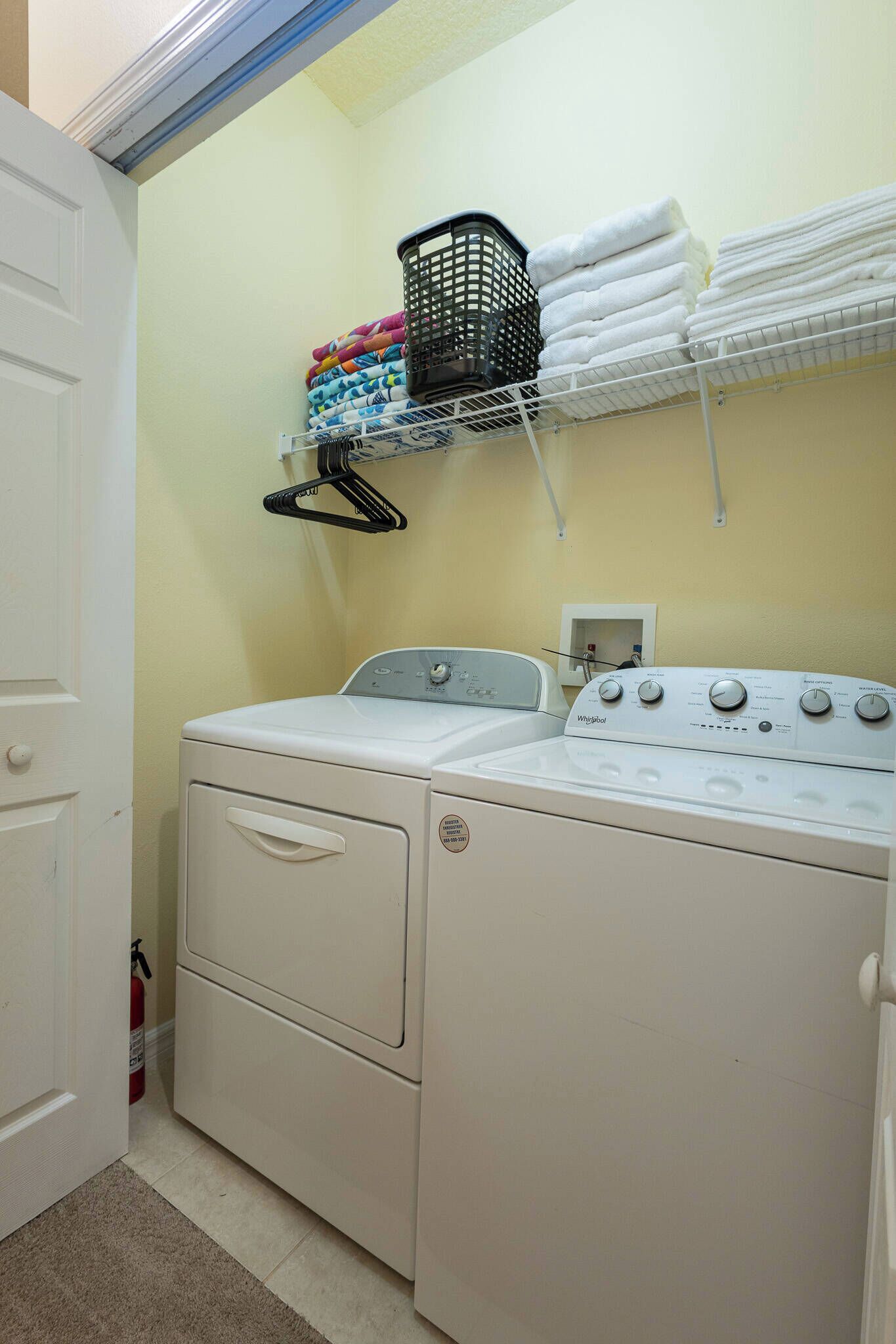 Un espace buanderie comprenant un lave-linge et un sèche-linge à chargement frontal, une étagère avec des serviettes pliées et un panier à linge.