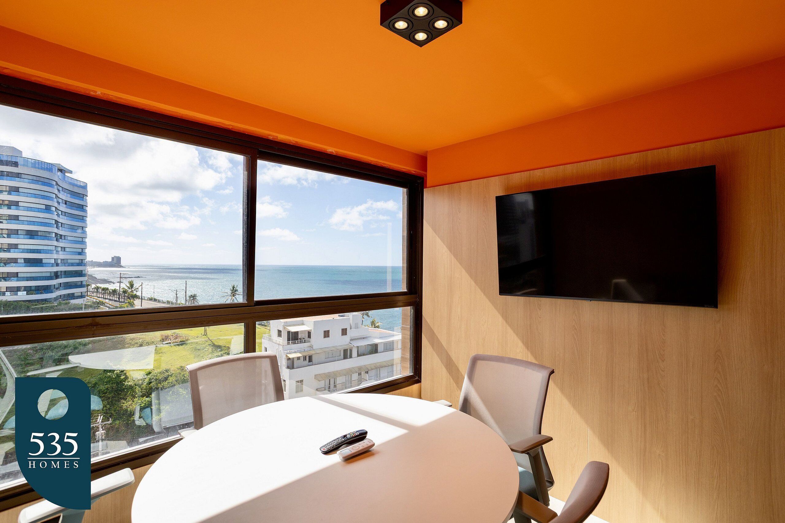Een moderne hotelkamer met een groot raam met uitzicht over de stad, een ronde tafel met stoelen, en een flatscreen tv aan de muur.