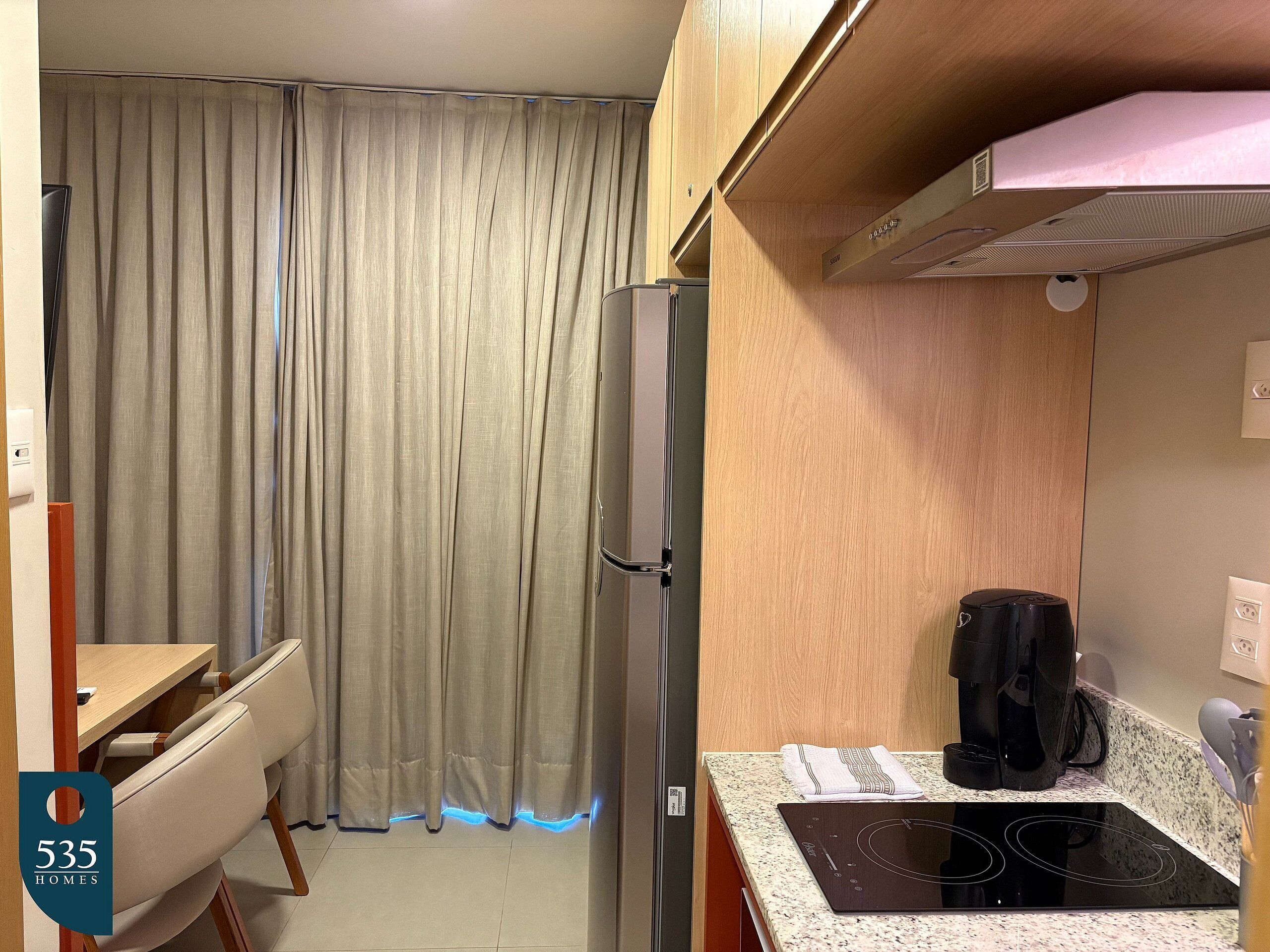 Una cocina compacta con refrigerador integrado, una encimera con placa de inducción y una zona de comedor con mesa y sillas.