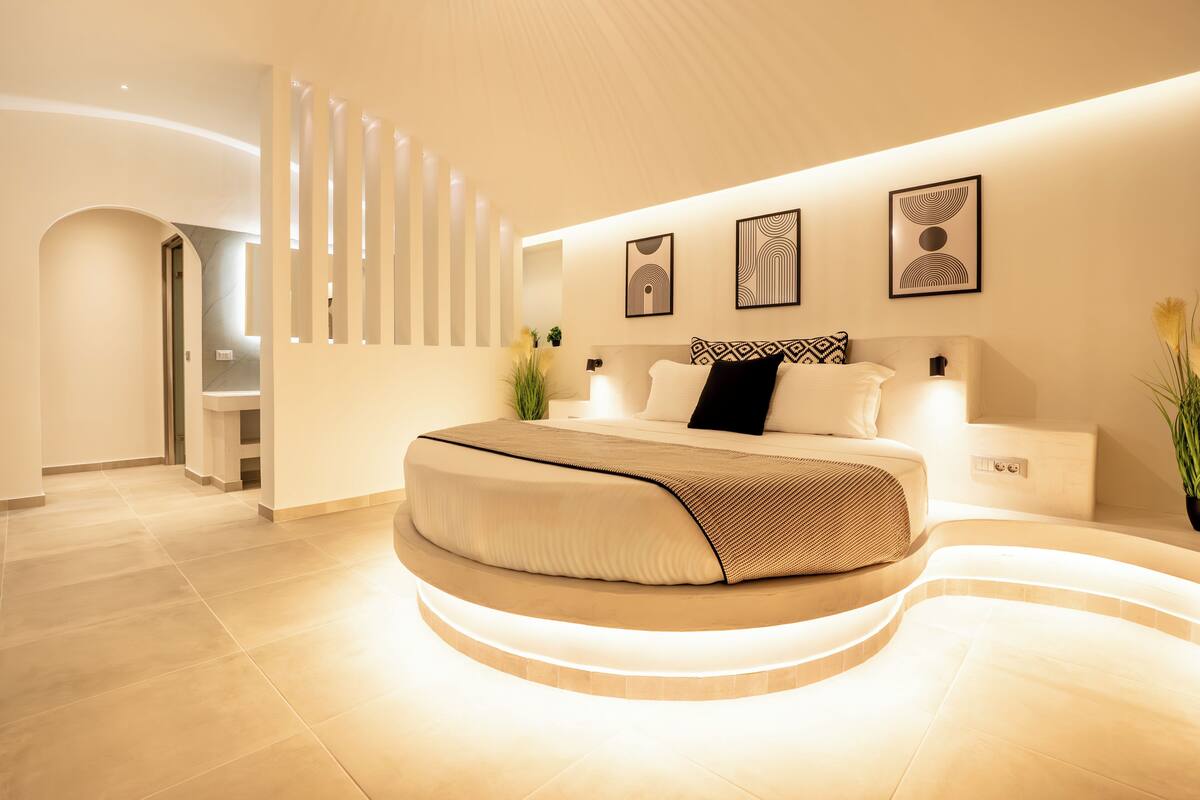 Une chambre moderne avec un lit aux lignes courbes, un téléviseur fixé au mur et un escalier.
