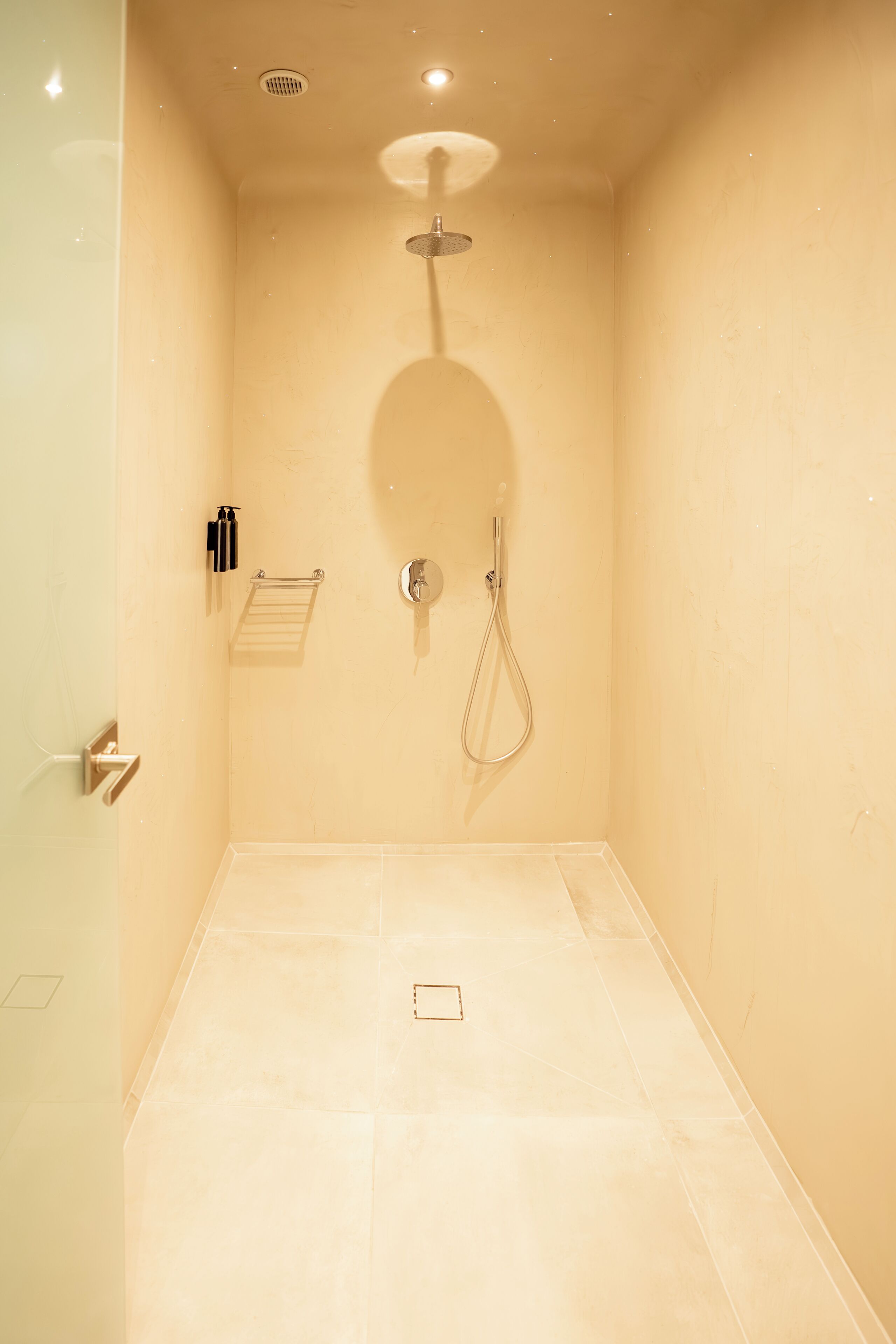 Un petit espace douche fermé, équipé d’un pommeau de douche à main et d’un robinet fixé au mur.