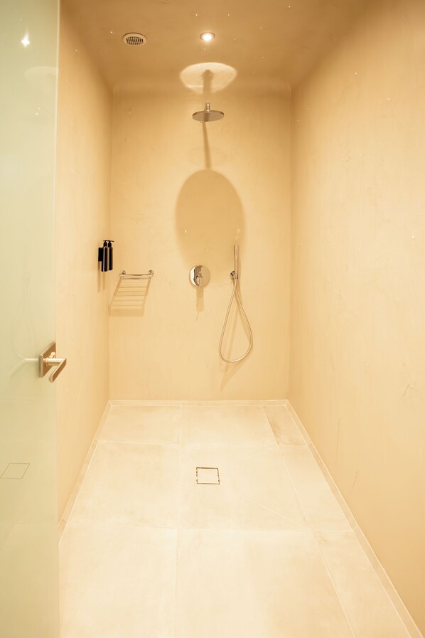 A small, enclosed shower area with a handheld showerhead and a wall-mounted faucet. - Santorini Cave Luxury Suites (Santorini)