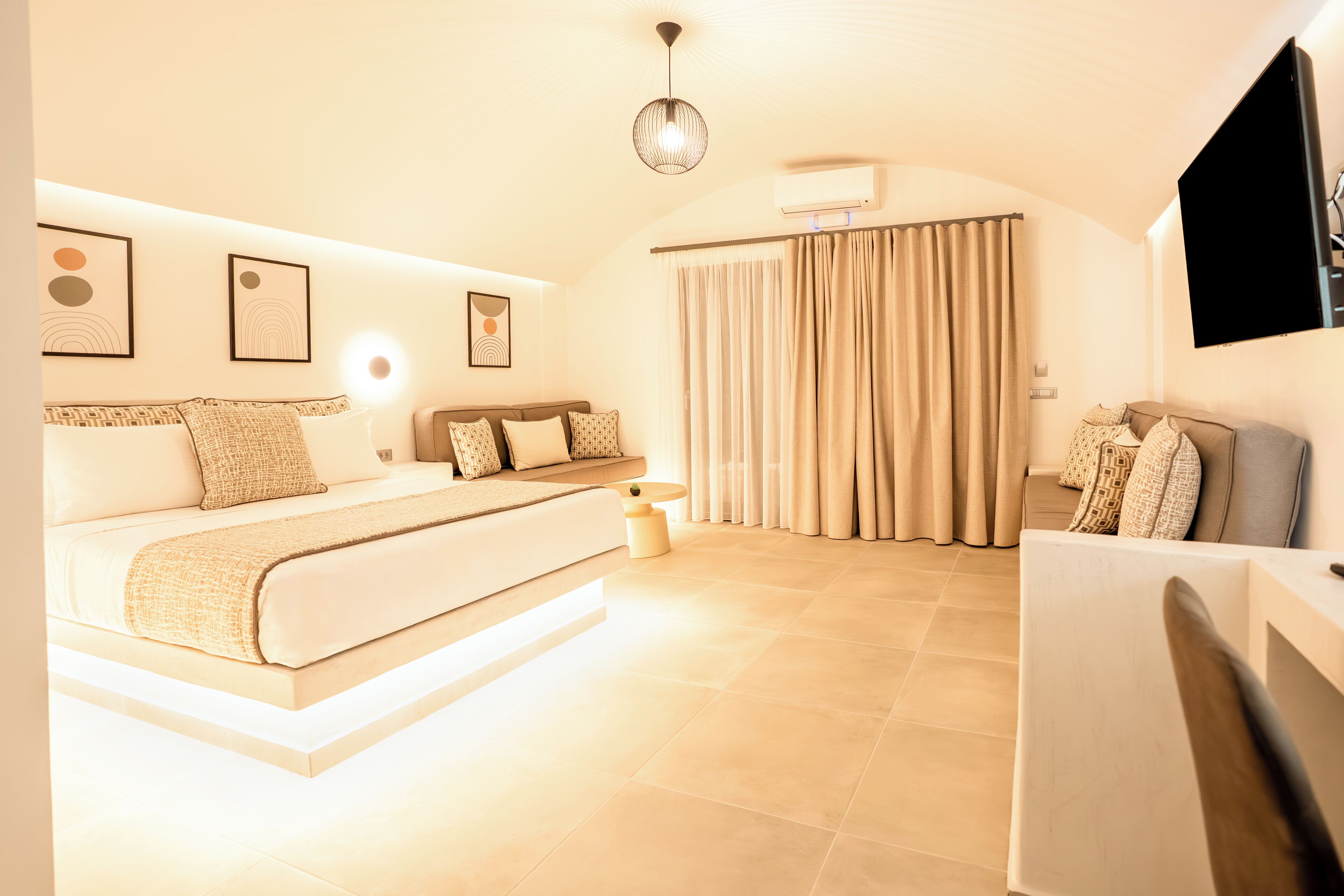 Un dormitorio moderno con una cama grande, una mesita de noche, una lámpara colgante y un televisor montado en la pared.