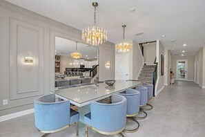 A modern dining area with a glass table, blue upholstered chairs, and a chandelier. - EV_2818 - 9 Bed 6 Bath Villa with Screened-In Private Pool with Spillover Spa, K (Kissimmee)
