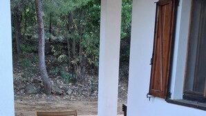 Ein Holztisch mit Stühlen steht auf einer gefliesten Terrasse mit Blick auf Bäume und ein Gebäude.