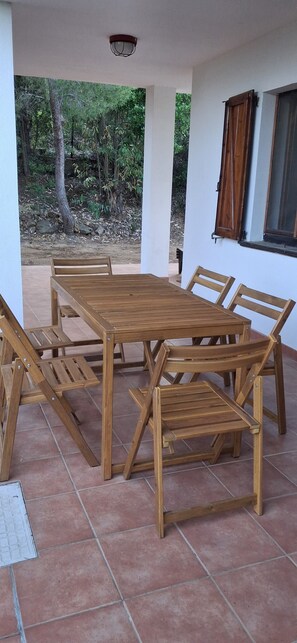 A wooden table and chairs set on a tiled patio with a view of trees and a building. - Apartment in Del Mirto Holiday House with terrace overlooking the sea of Nora (villa San Pietro Cagliari)
