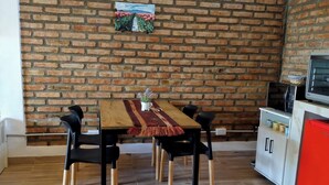 A dining area with a brick wall, a table with chairs, and a kitchen area with appliances. - Warm and modern apartment (Esquel)