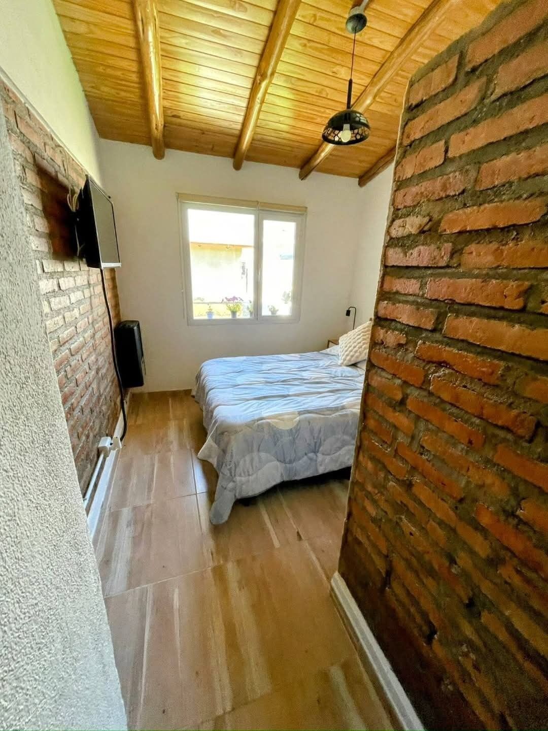 Ein schmales Zimmer mit Bett, Fenster und Backsteinwand.