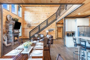 A spacious living area with a fireplace, a dining table set for six, a staircase, and a kitchen with white cabinets. - Beautiful 5-bedroom cabin with AC in peaceful Sevierville (Sevierville)