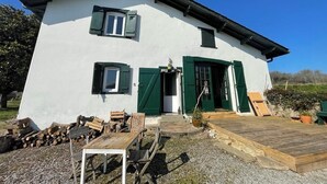 En hvid bygning med grønne skodder, en træterrasse og en grusindkørsel.