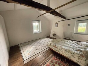Une chambre à coucher avec un lit, deux fenêtres, un radiateur et une poutre en bois au plafond.