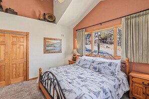 Ein Schlafzimmer mit Bett, Holzschrank, einem Gemälde, einem Fenster mit Vorhängen und Blick nach draußen.