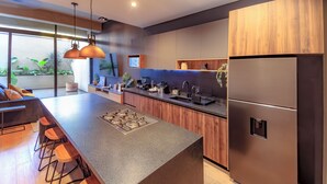 A modern kitchen with a large island, bar stools, a stainless steel refrigerator, and wooden cabinetry. - Atena Urban Living (Guadalajara)