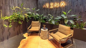 A modern lobby with two leather armchairs, a round side table, and a wooden wall with 'ATENA' illuminated letters. - Atena Urban Living (Guadalajara)