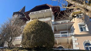 A multi-story building with balconies, a large central tree, and snow on the ground. - Vacation apartment Alpenglühen - Untersberg view (Berchtesgaden)