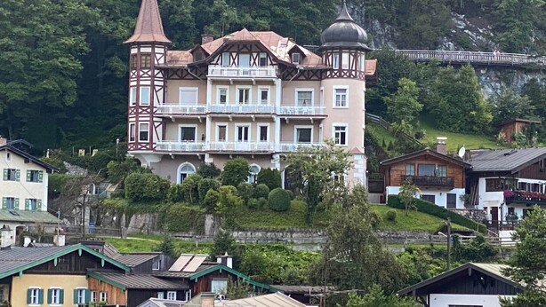 A multi-story building with a turret and a dome, surrounded by lush greenery and other residential buildings. - Vacation apartment Alpenglühen - Untersberg view (Berchtesgaden)