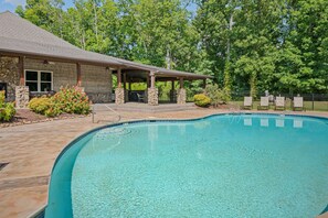 Une piscine dotée d’un patio couvert, de murs en pierre et offrant une vue sur les arbres.