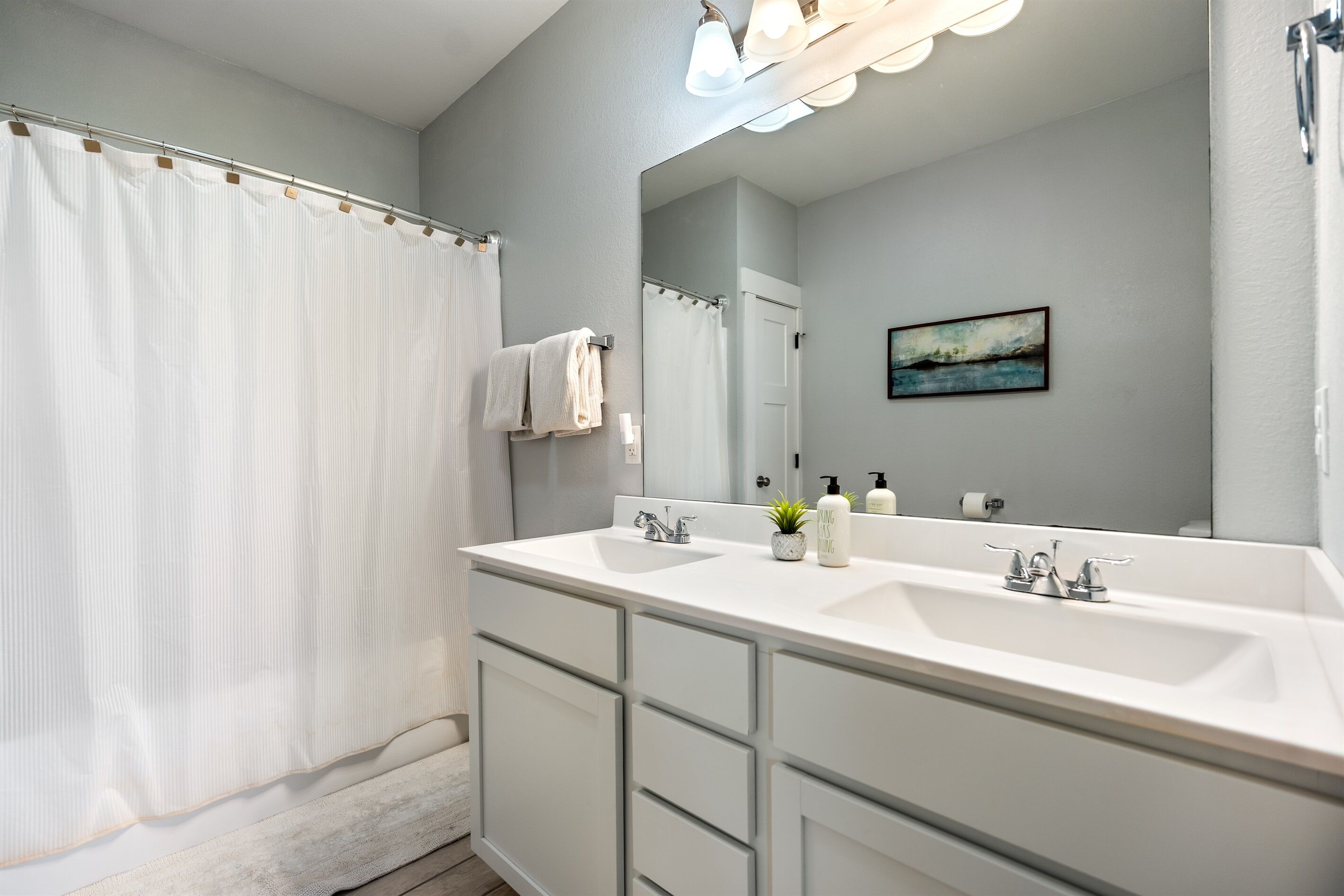 A modern bathroom with a large mirror, two sinks, and a shower curtain.
