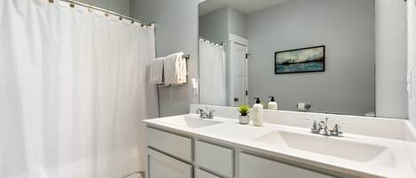 A modern bathroom with a large mirror, two sinks, and a shower curtain.