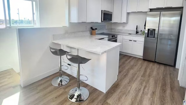 Una cucina moderna con mobili bianchi, elettrodomestici in acciaio inossidabile e un'isola centrale con sgabelli da bar.