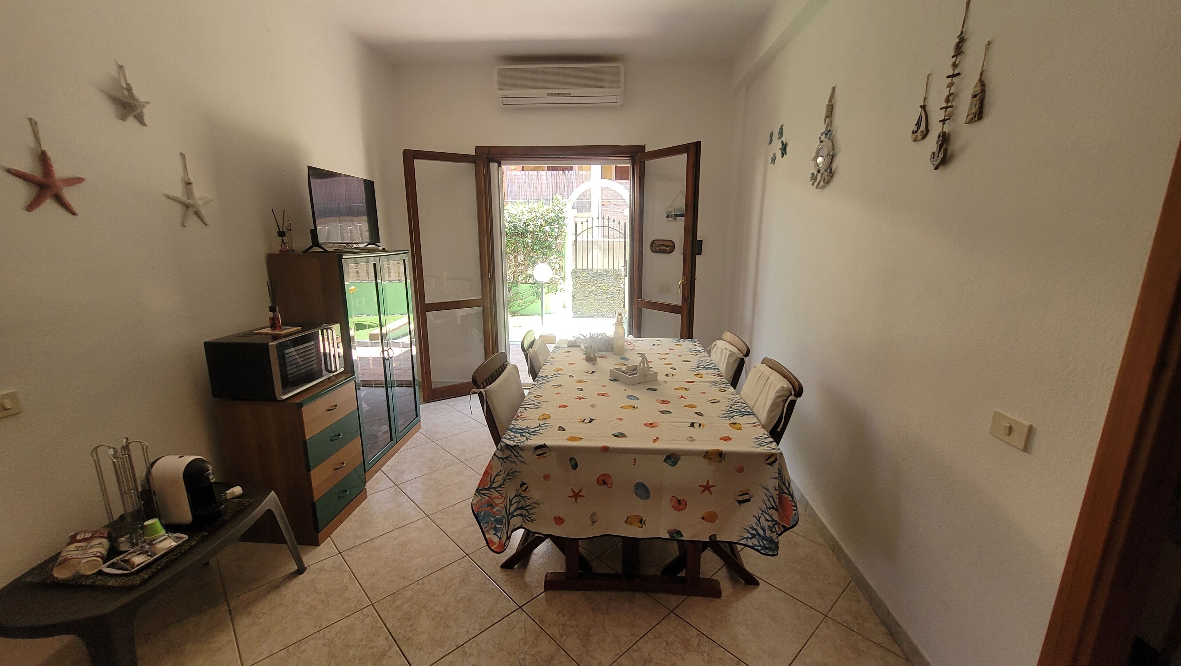 A dining area with a table set for four, a cabinet with a television, and a door leading outside.