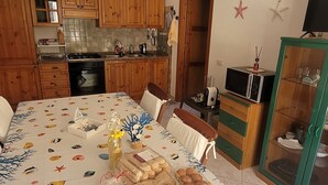 A kitchen with wooden cabinets, a dining table with a fish-themed tablecloth, and a TV on a stand. - Villa with garden in Villasimius (Cagliari)
