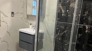 A modern bathroom with a glass shower enclosure, a vanity with a sink, and marble-patterned walls. - Potters Hideout (Watford)