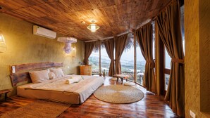 Een kamer met een houten plafond, een bed met een groot raam, een kleine tafel en uitzicht op het landschap.