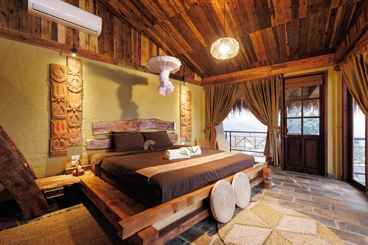 Une chambre à coucher avec un cadre en bois, un grand lit, un luminaire suspendu et une vue par la fenêtre.