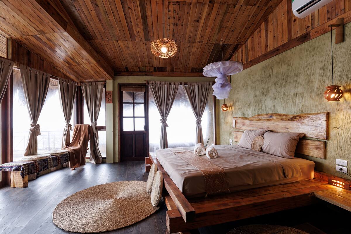 Une pièce en bois avec un lit, des rideaux, un banc et un tapis tissé.