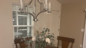 A dining room with a wooden table, four chairs, a vase with flowers, and a chandelier. - Centrally Located close to Brownwood, Sawgrass and Eastport with Golf Cart. (The Villages)