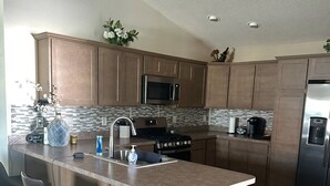 A modern kitchen with wooden cabinets, a central island with bar stools, stainless steel appliances, and a tiled backsplash. - Centrally Located close to Brownwood, Sawgrass and Eastport with Golf Cart. (The Villages)