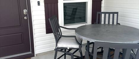 Eine Veranda mit rundem Tisch, vier Stühlen, einer Tür und einem Fenster mit Rollläden.